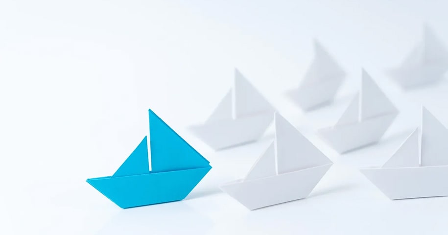 Blue origami boat leading other white paper boats