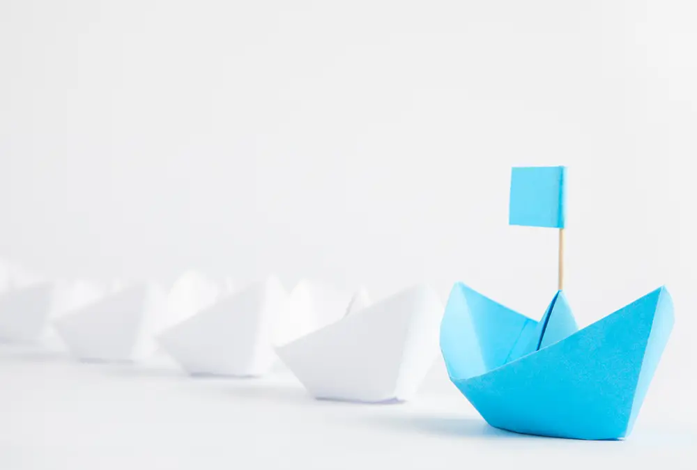 Blue origami boat sitting alongside other white paper boats